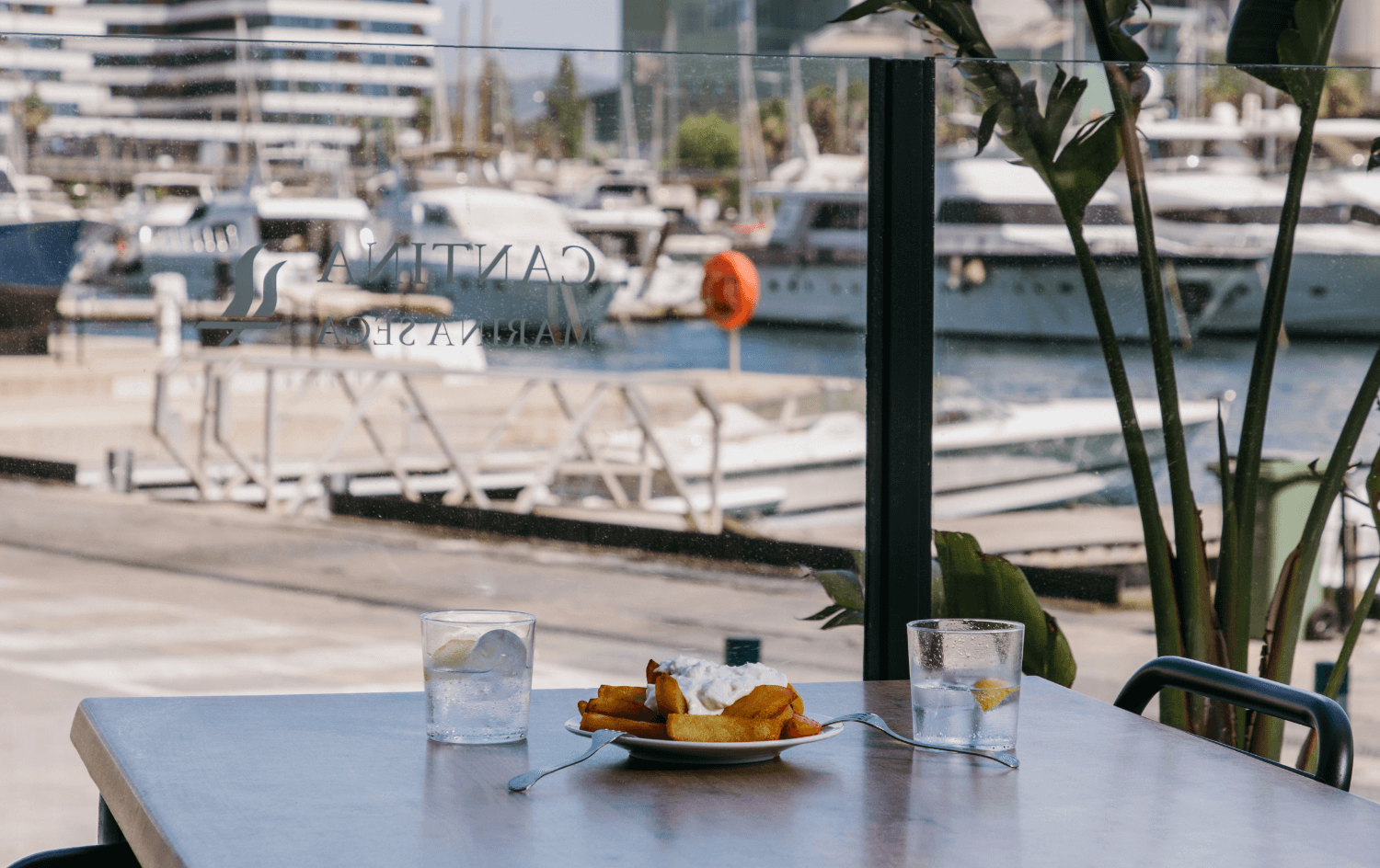 Plat amb postres i begudes en un balcó amb vistes al port.
